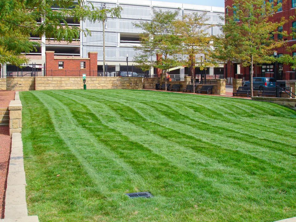 Freshly striped commercial courtyard lawn framed by brick paving, stone walls, and shade trees